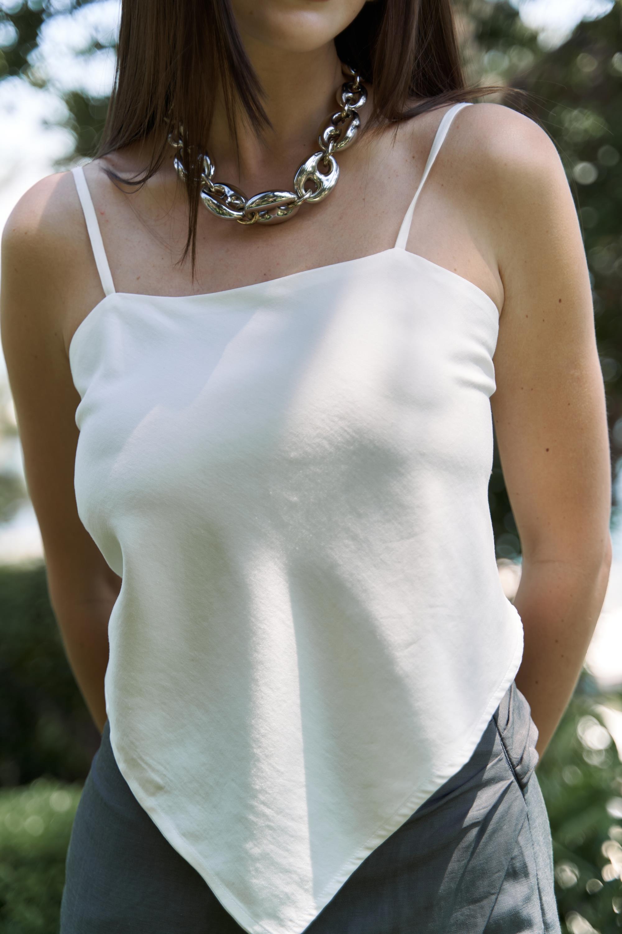 Person wearing a white tank top and dark pants with a blurred natural background