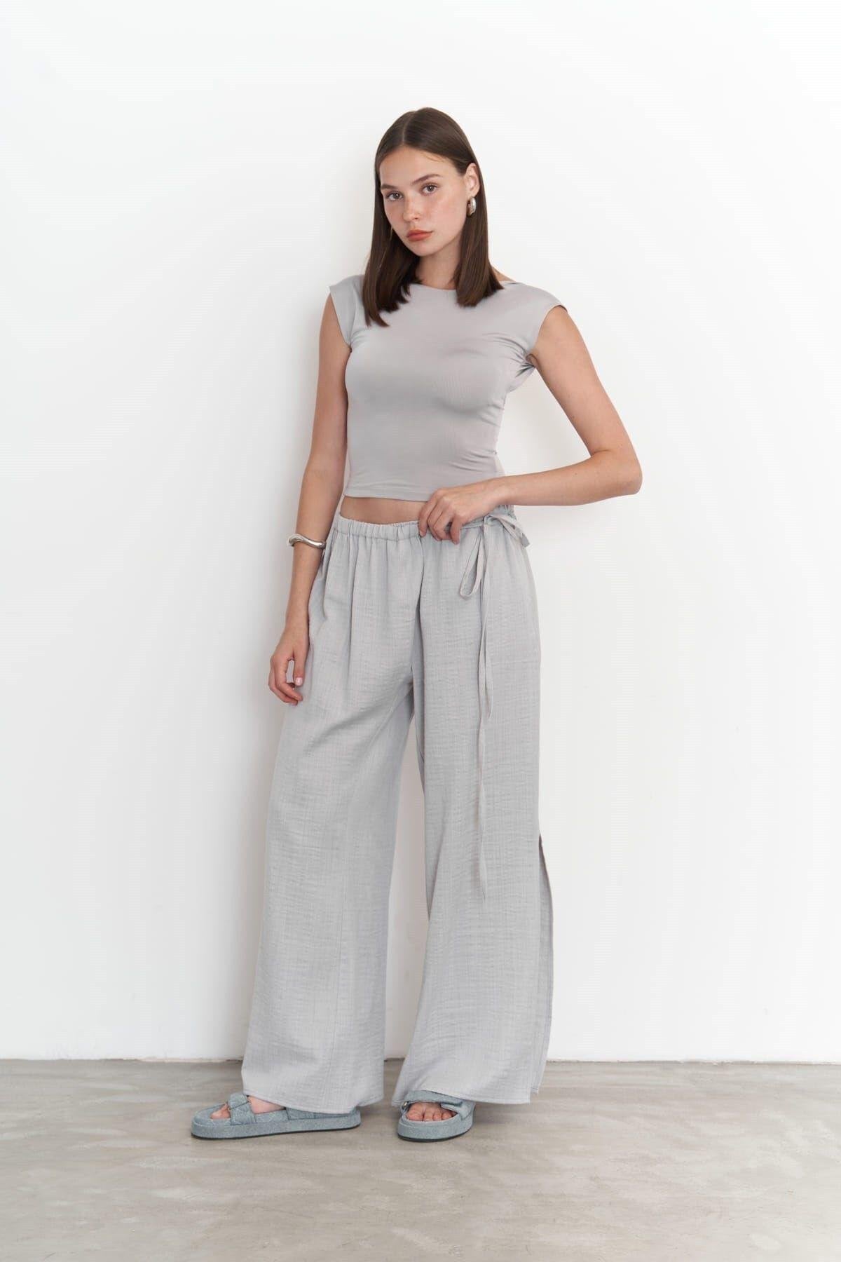 Woman wearing a gray sleeveless top and wide-leg pants against a white background