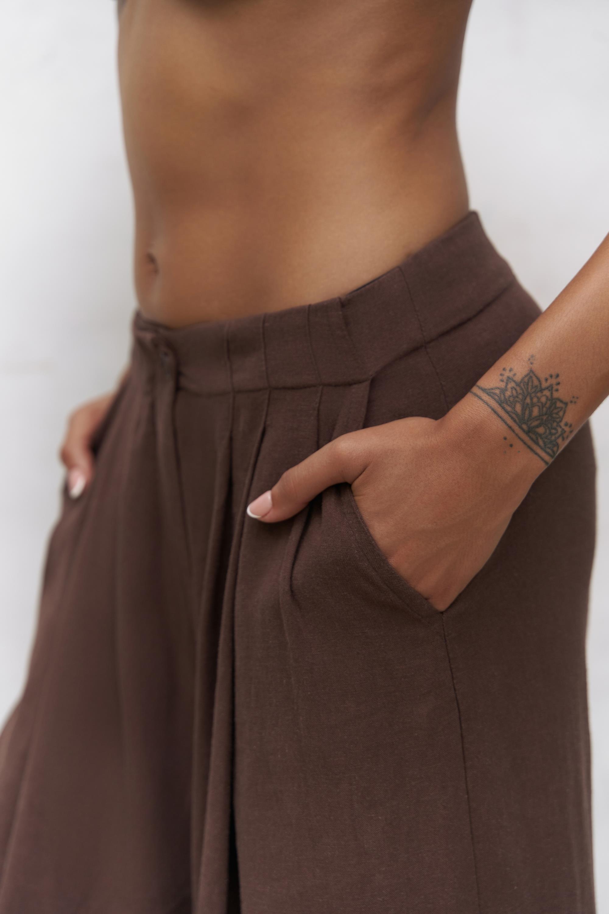 Model wearing brown linen blend trousers in resort setting – SHAÉN