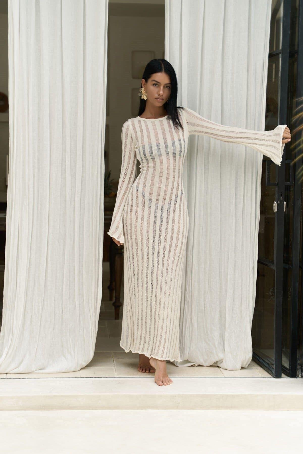 Model in see-through stripe knit dress with flared sleeves and maxi silhouette