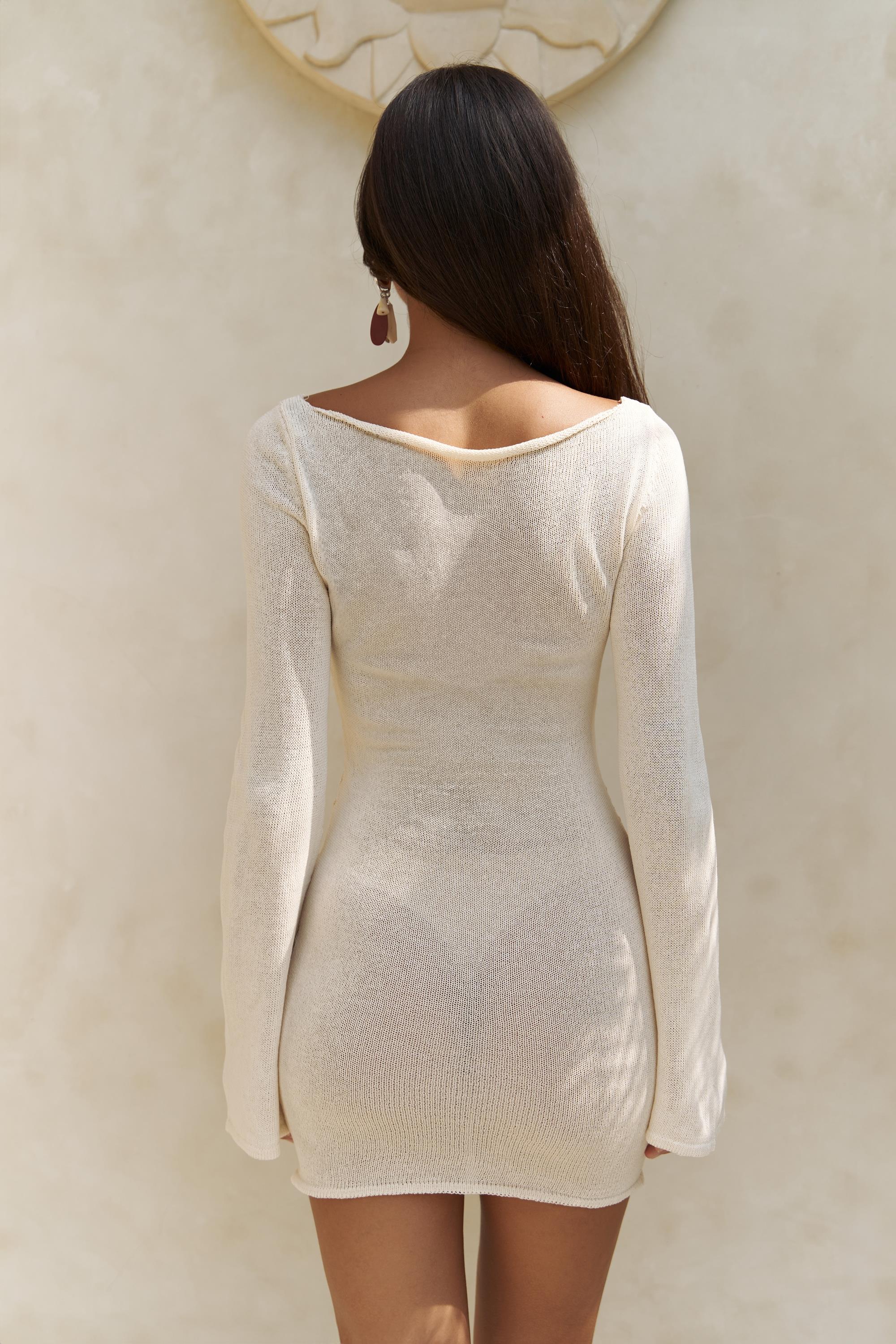 Woman wearing a white long-sleeve midi knit beach dress against a neutral background