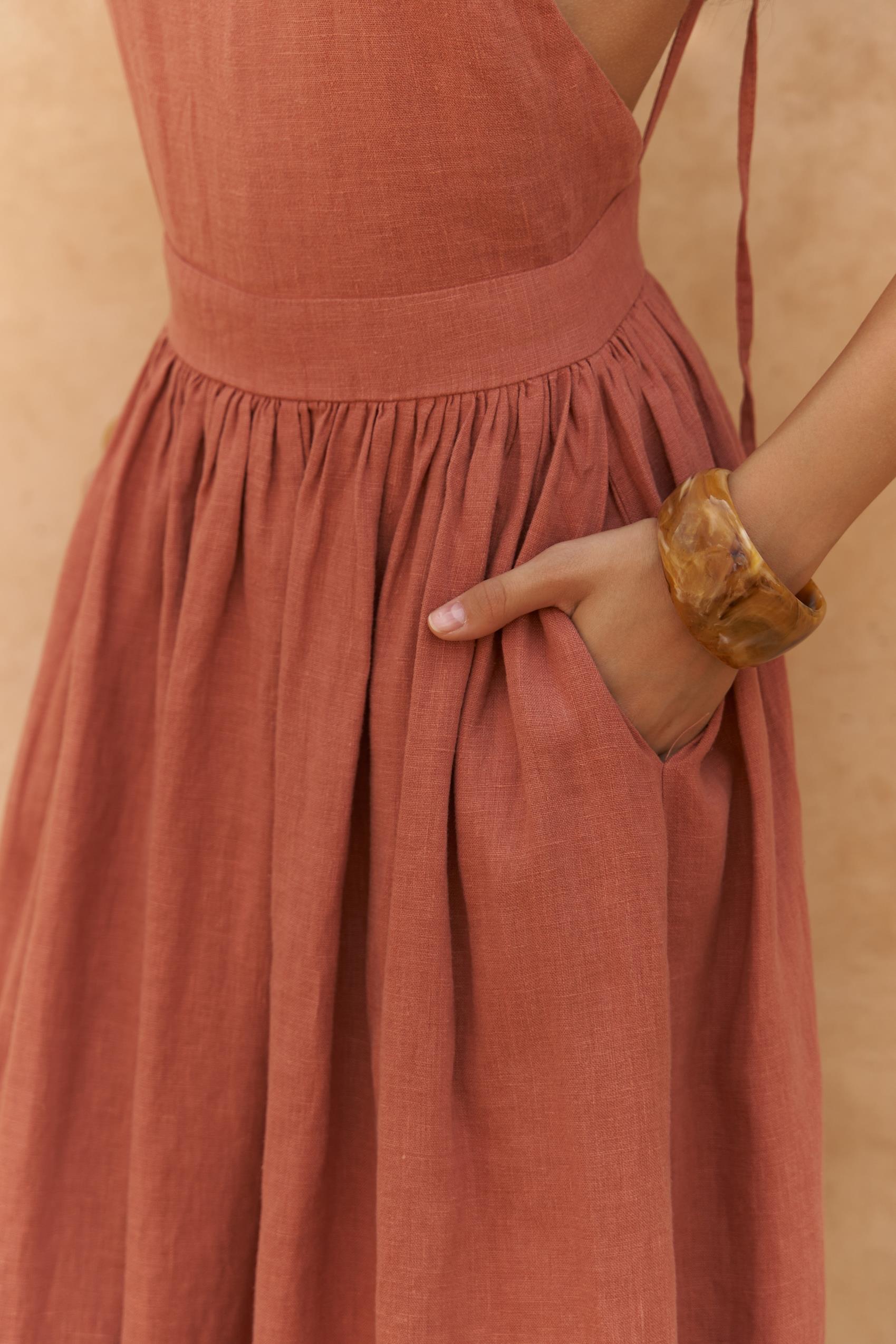 Person wearing a rust-colored linen midi dress with a plain background