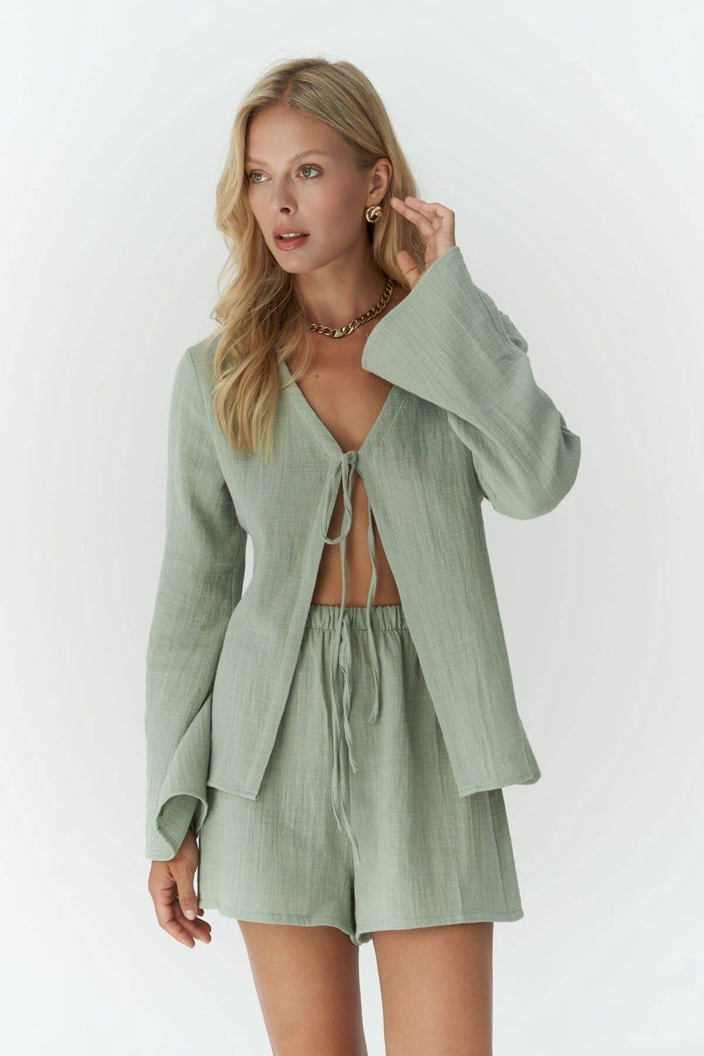 Woman wearing a light green outfit with a jacket and shorts on a white background