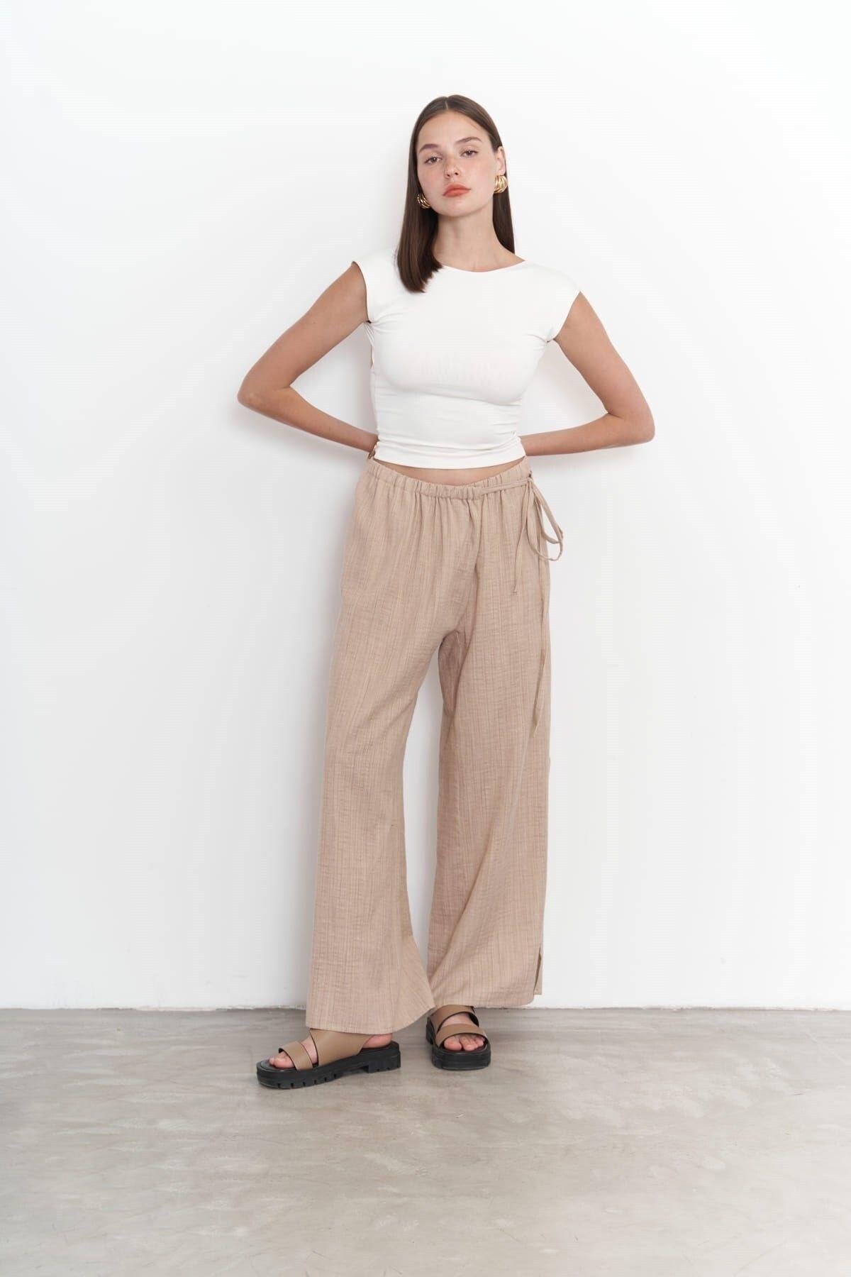 Model wearing beige wide-leg cotton-linen pants with side-tie detail