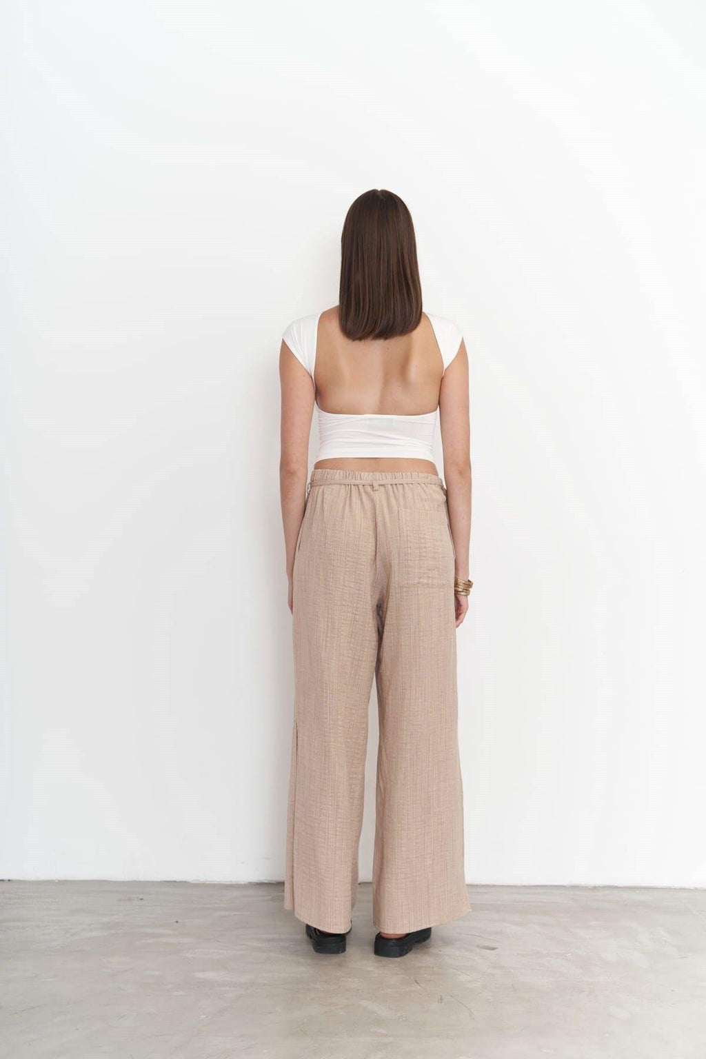 Woman wearing a white top and beige wide-leg pants against a white wall.
