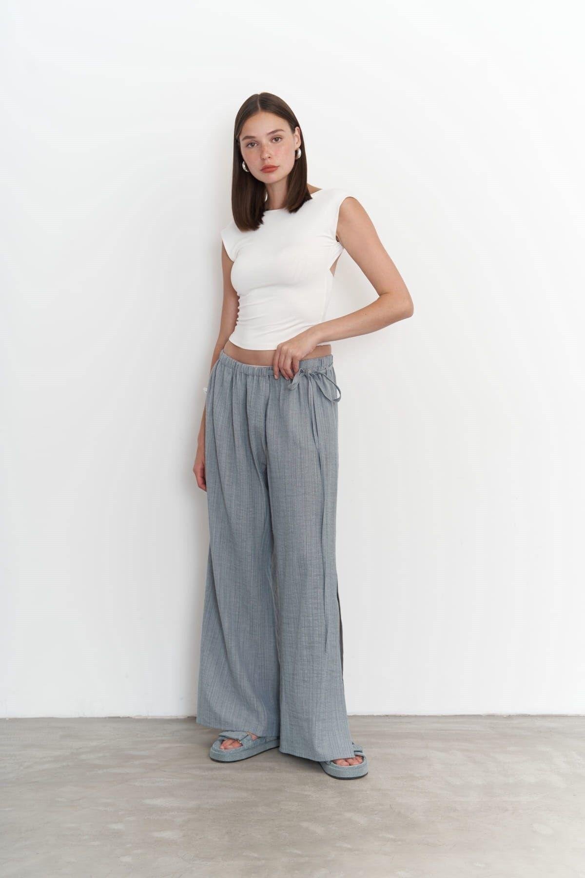 Woman wearing a white top and gray wide-leg pants against a white background