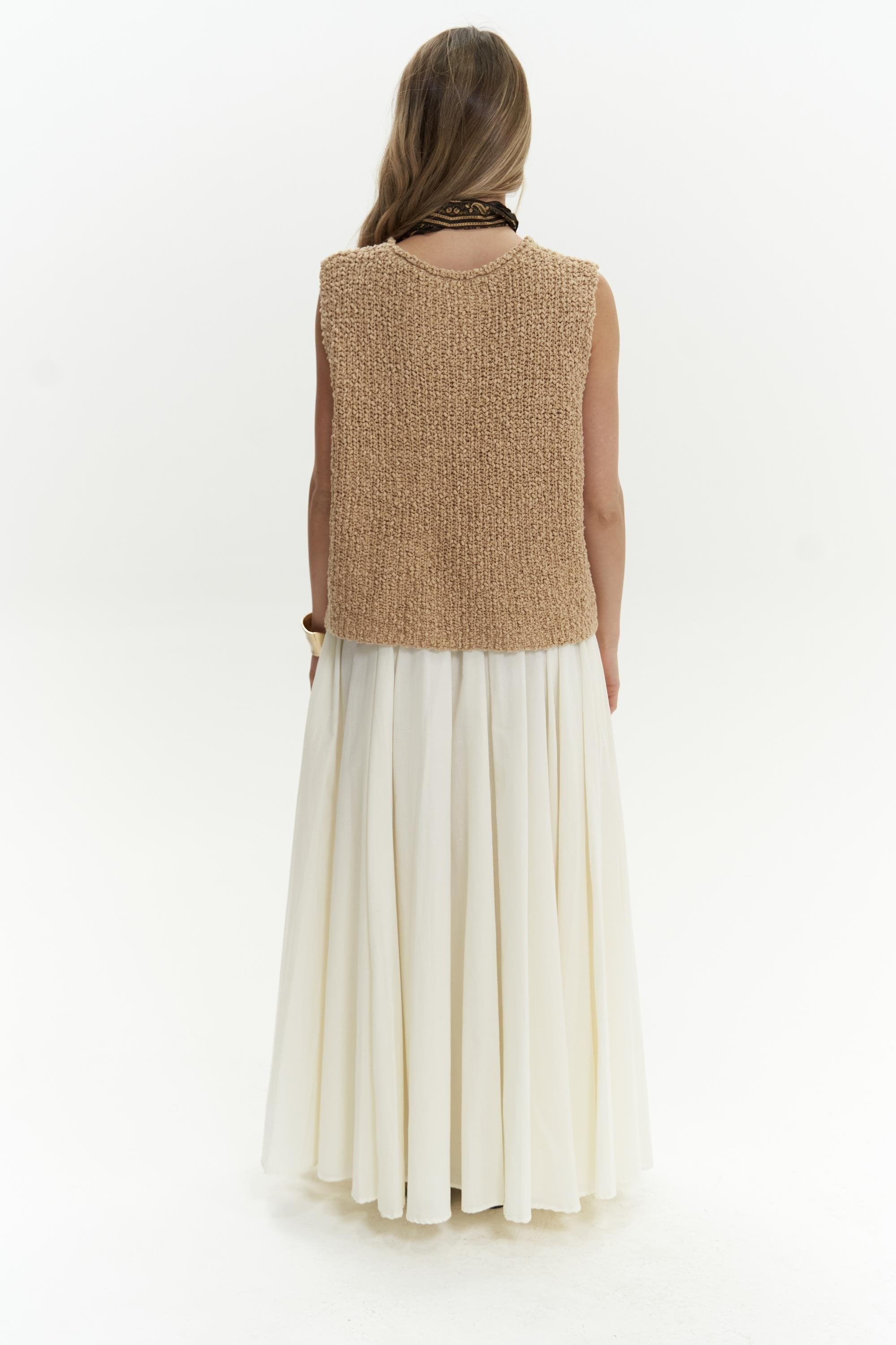 Woman wearing a beige knitted vest over a white dress on a white background