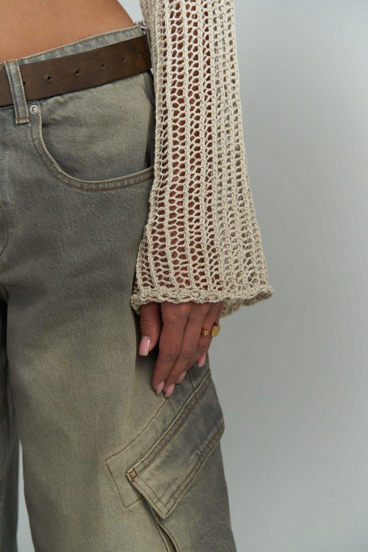 Person wearing a beige knit crochet over a green shirt with a neutral background