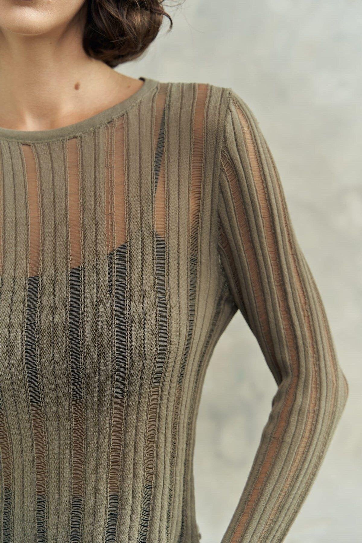 Close-up of a person wearing a olive color ribbed sheer knit  top with a neutral color palette.