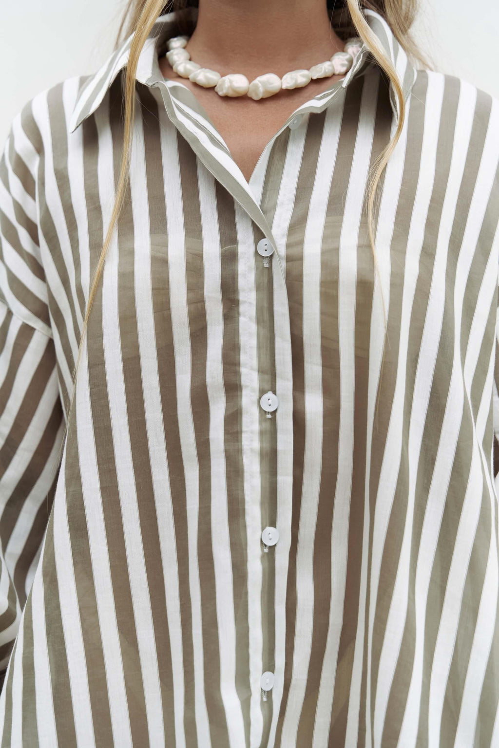 Close-up of a person wearing a striped cotton shirt with a pearl necklace.