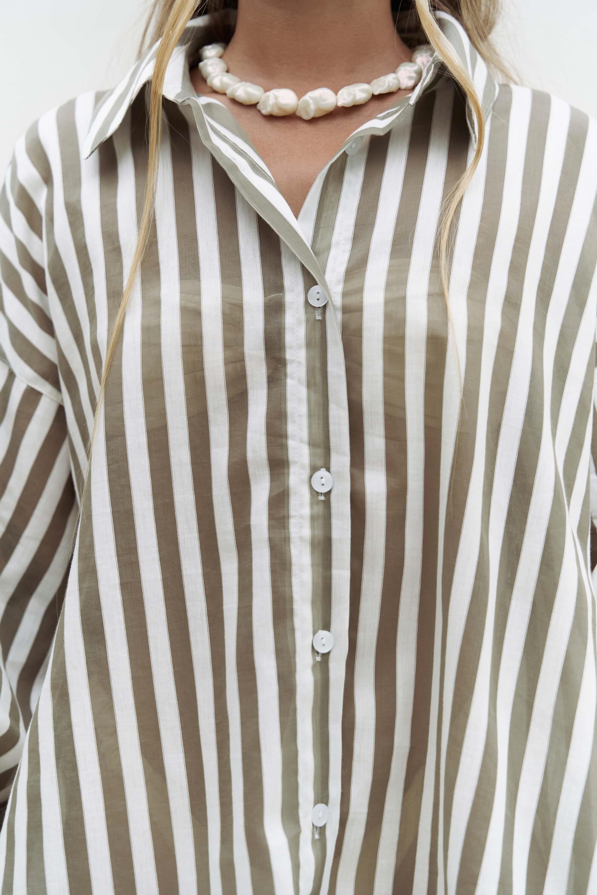 Close-up of a person wearing a striped cotton shirt with a pearl necklace.