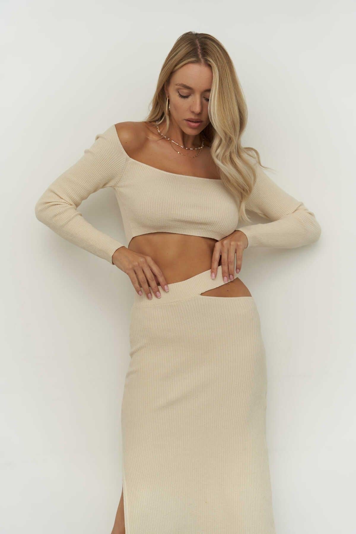 Woman wearing a beige long-sleeve top and skirt set against a white background